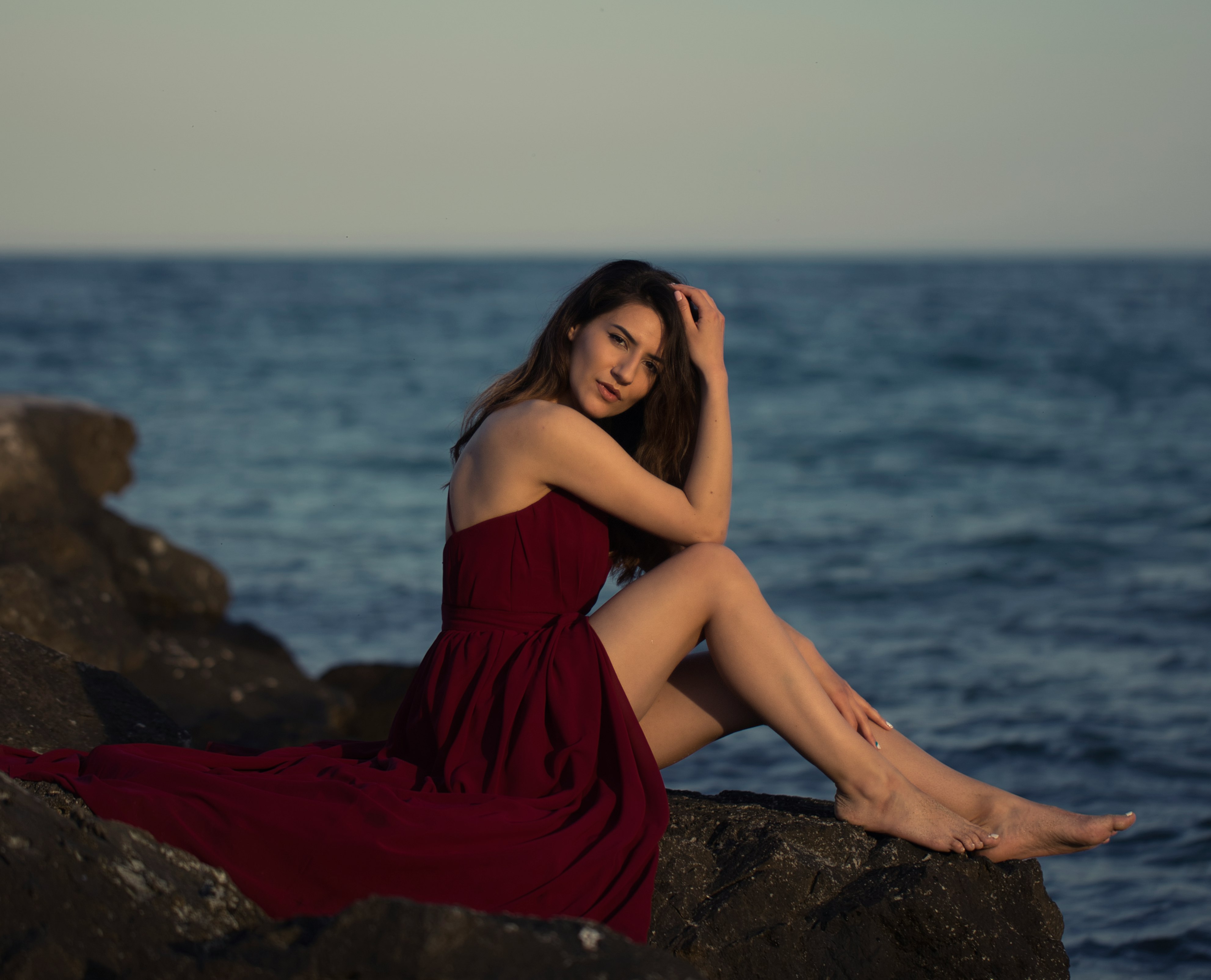 woman in red dress sitting on rock near sea during daytime